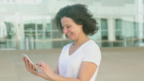 Smiling-mature-woman-using-smartphone-on-street.